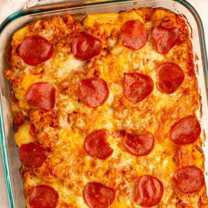 Baked biscuit pizza casserole is topped with melted mozzarella and turkey pepperoni in a glass baking dish.