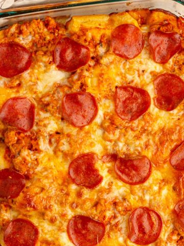 Baked biscuit pizza casserole is topped with melted mozzarella and turkey pepperoni in a glass baking dish.