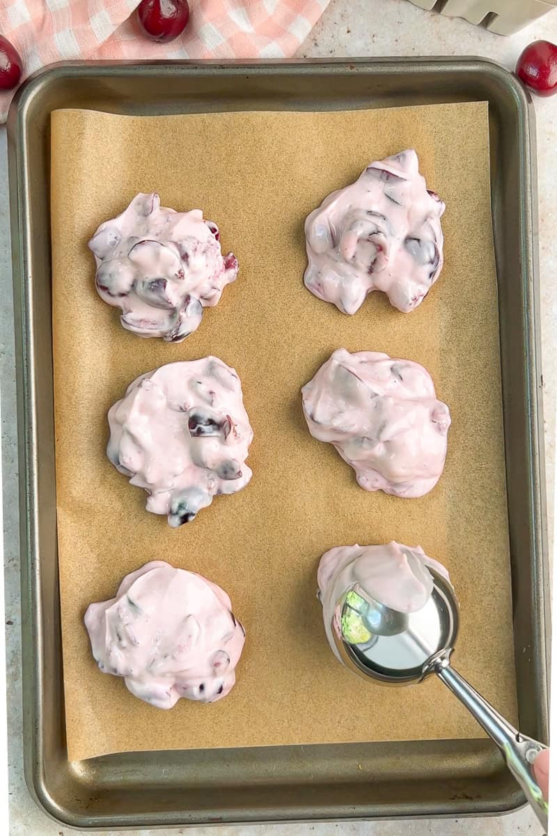 Cherry yogurt mixture is scooped onto a parchment-lined baking sheet.