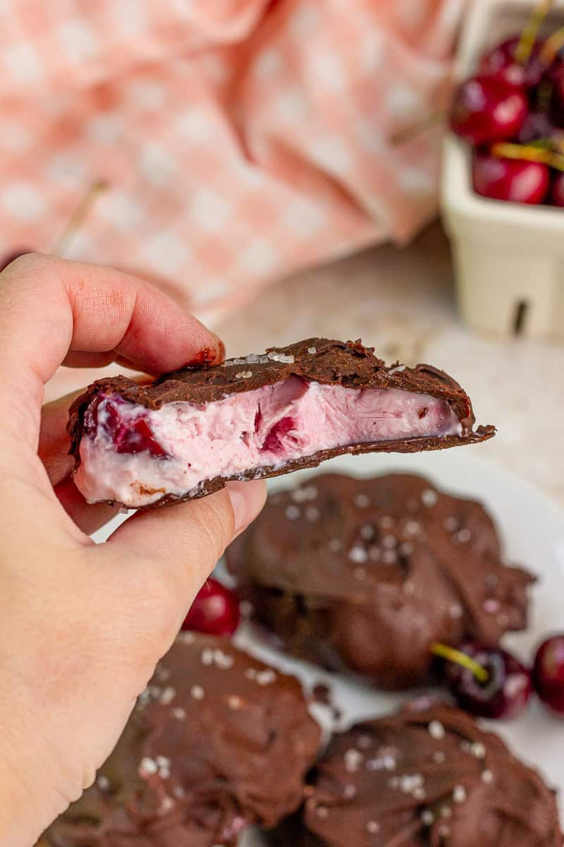 A hand holds a chocolate covered frozen yogurt bite with creamy cherry filling.