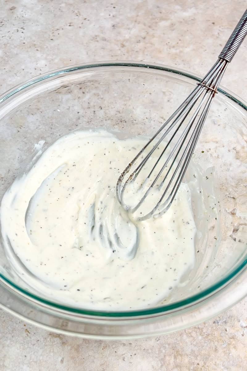 Ranch dressing ingredients are whisked together in a glass mixing bowl.