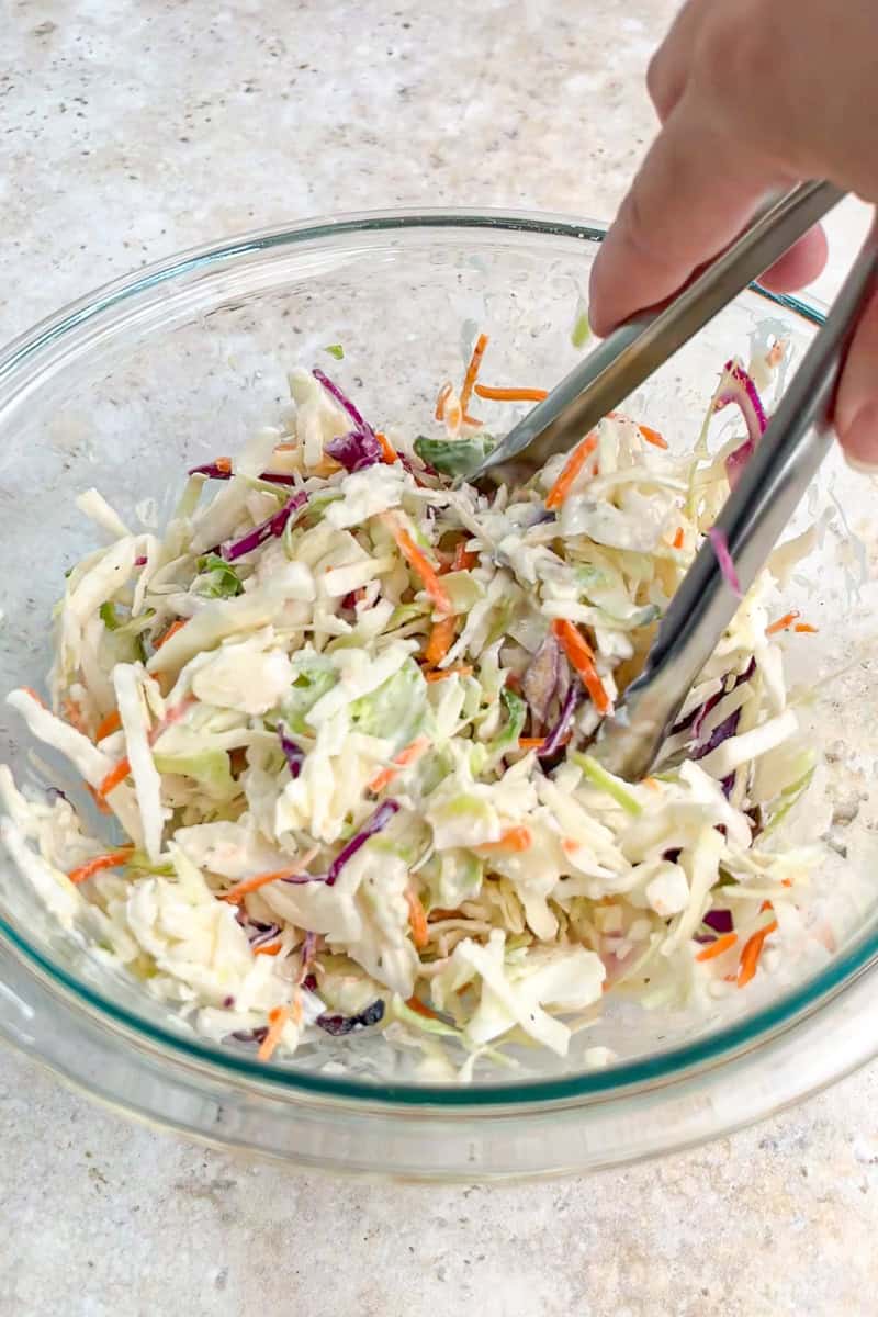 Tri-color coleslaw mix is tossed in creamy ranch dressing in a glass bowl.