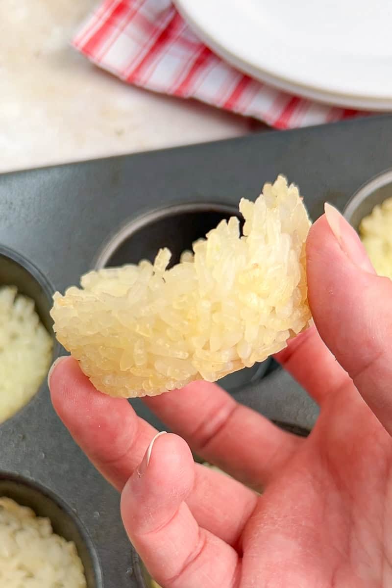 A baked short-grain rice cup is held by hand to show its crispy edges and sturdy shape.