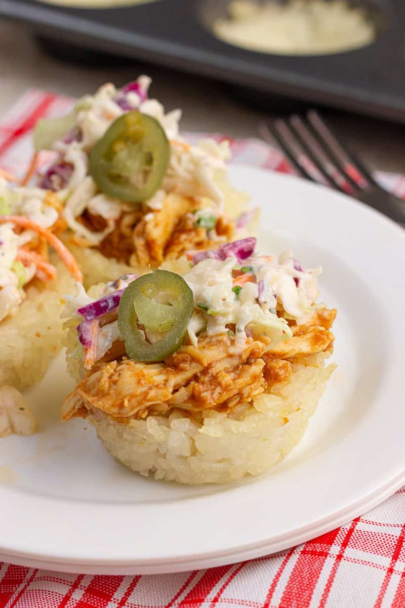 BBQ chicken crispy rice cups topped with ranch coleslaw and pickled jalapeños on a white plate.