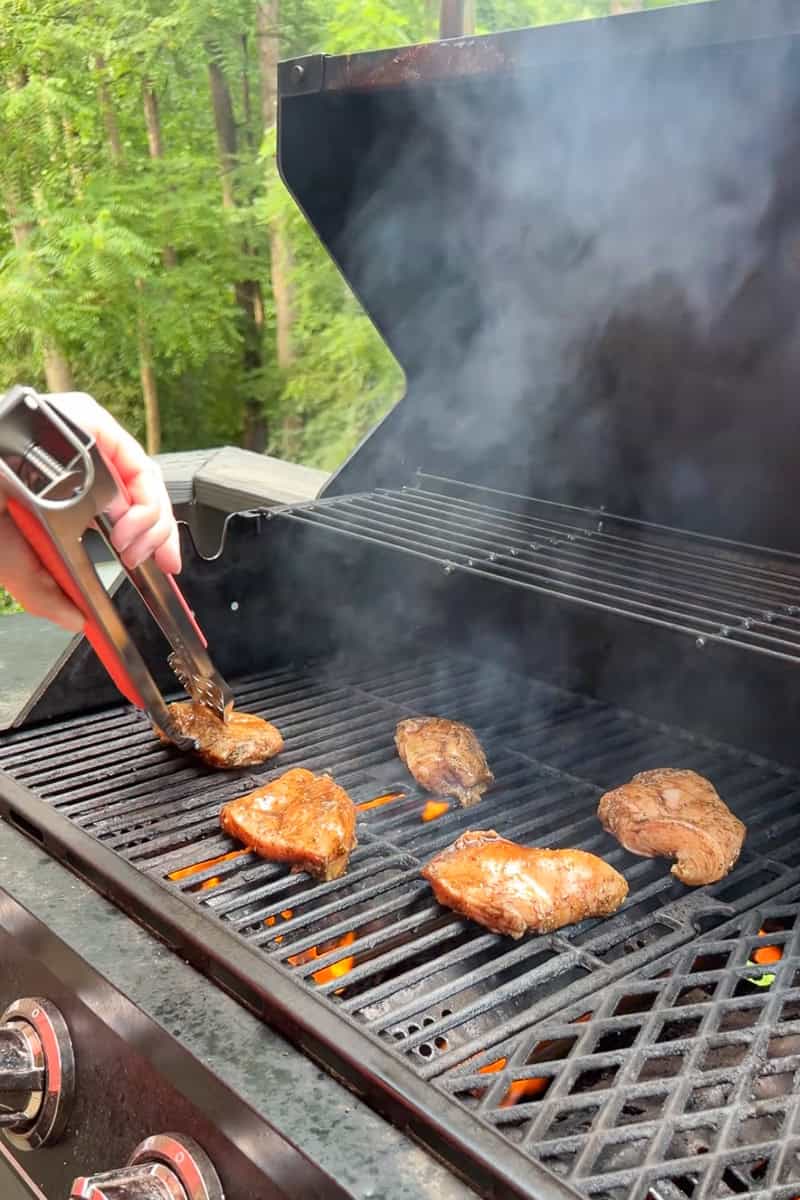 Marinated chicken breasts are placed on a hot grill with flames and smoke.