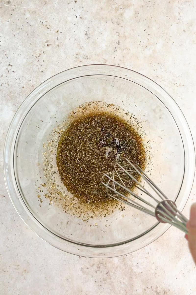 Balsamic chicken marinade is whisked together in a glass bowl with Italian seasoning and garlic.