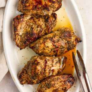 Grilled balsamic chicken breasts are arranged on a white platter with golden pan juices.