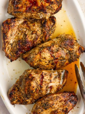 Grilled balsamic chicken breasts are arranged on a white platter with golden pan juices.