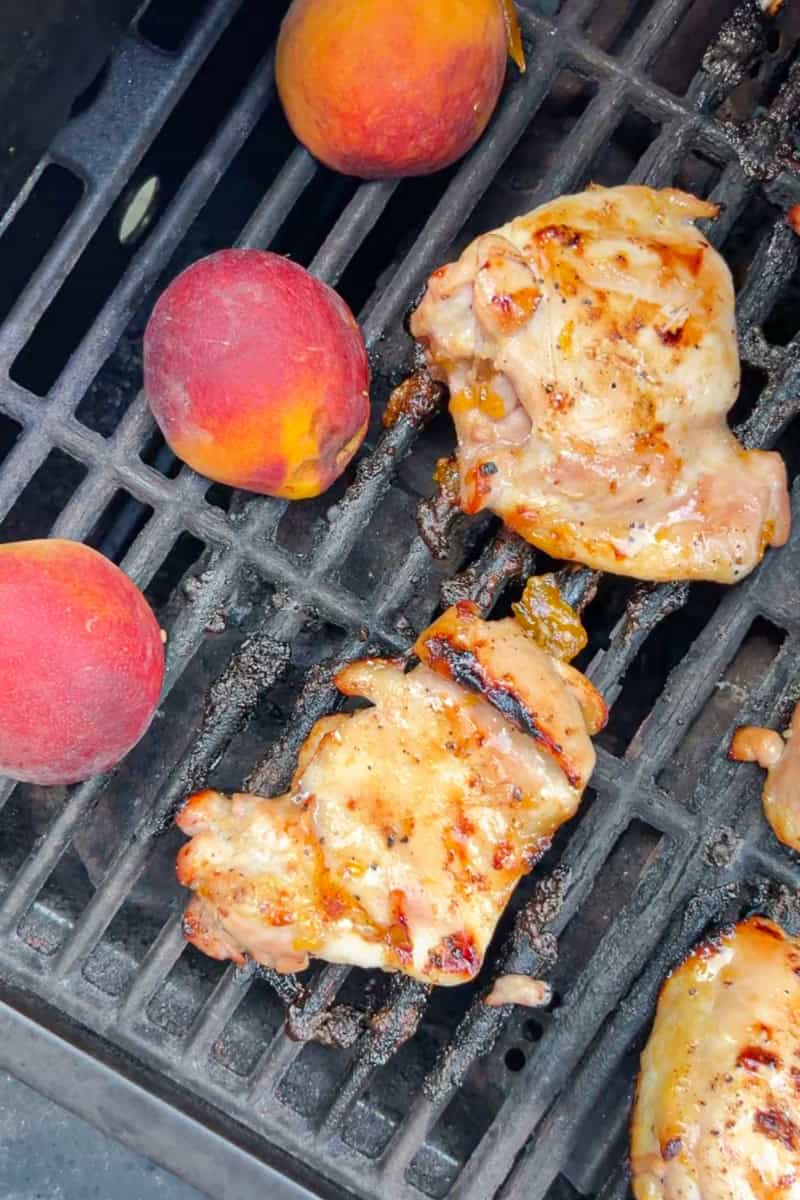 Chicken thighs and whole peaches cook together on a hot grill.