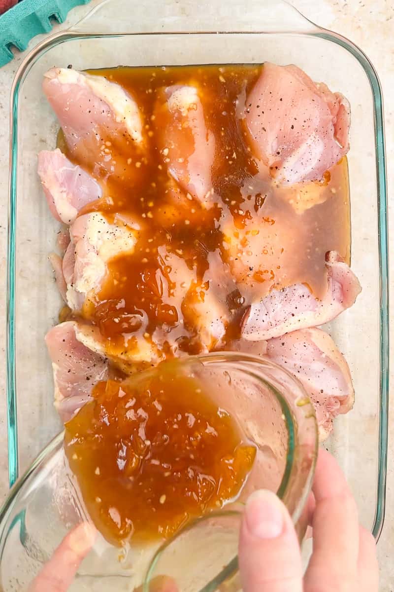 Peach marinade is poured over raw chicken thighs in a glass baking dish.