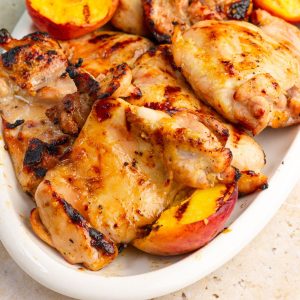Grilled peach chicken thighs and charred peaches are served on a white platter.