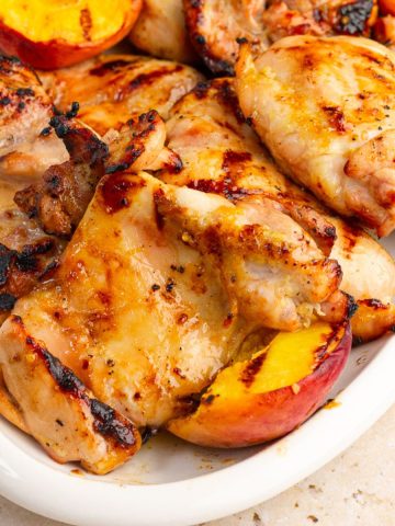 Grilled peach chicken thighs and charred peaches are served on a white platter.
