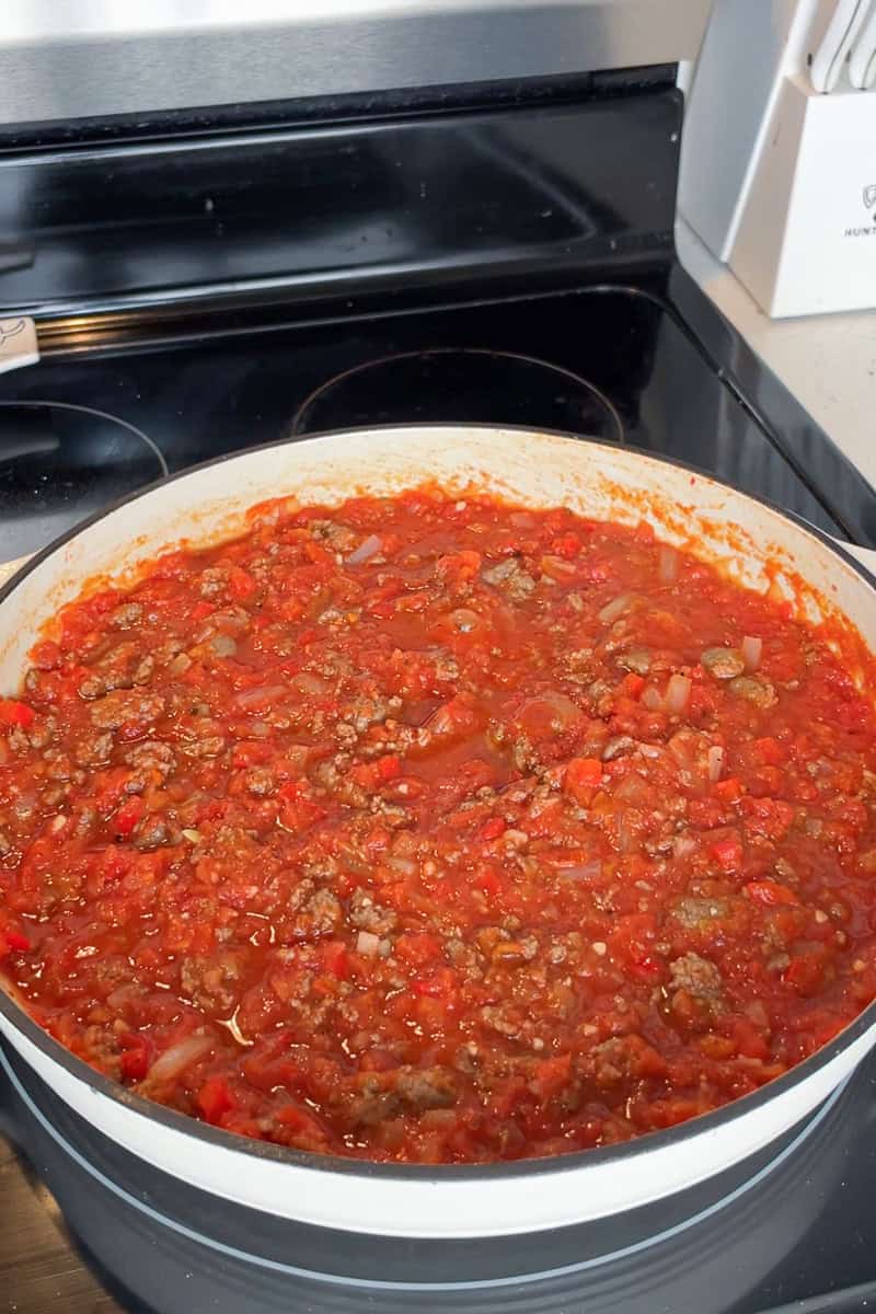 Tomato sauce with turkey sausage, onion, and red bell pepper simmers in a skillet.