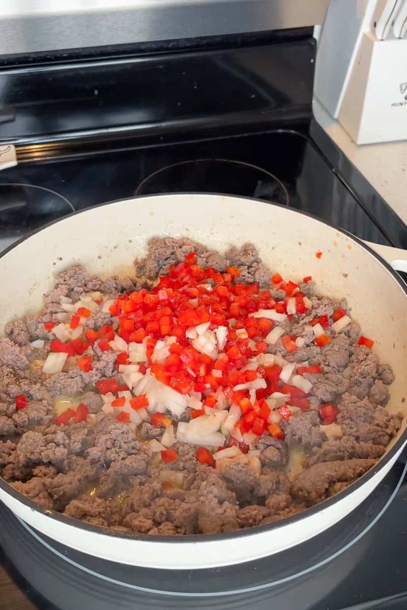 Diced onion and red bell pepper are added to cooked turkey sausage in a skillet.