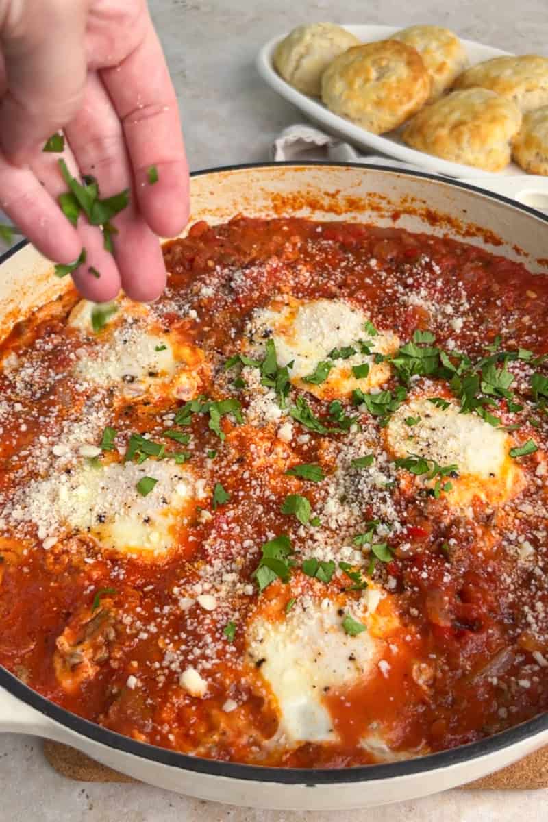 Fresh parsley is sprinkled over a finished skillet of high protein shakshuka served with biscuits.