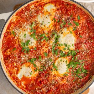 A skillet of high protein shakshuka is topped with cheese and parsley.