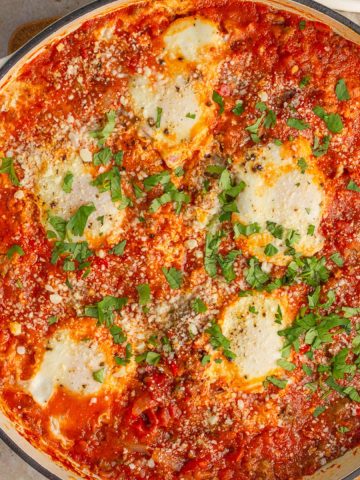 A skillet of high protein shakshuka is topped with cheese and parsley.