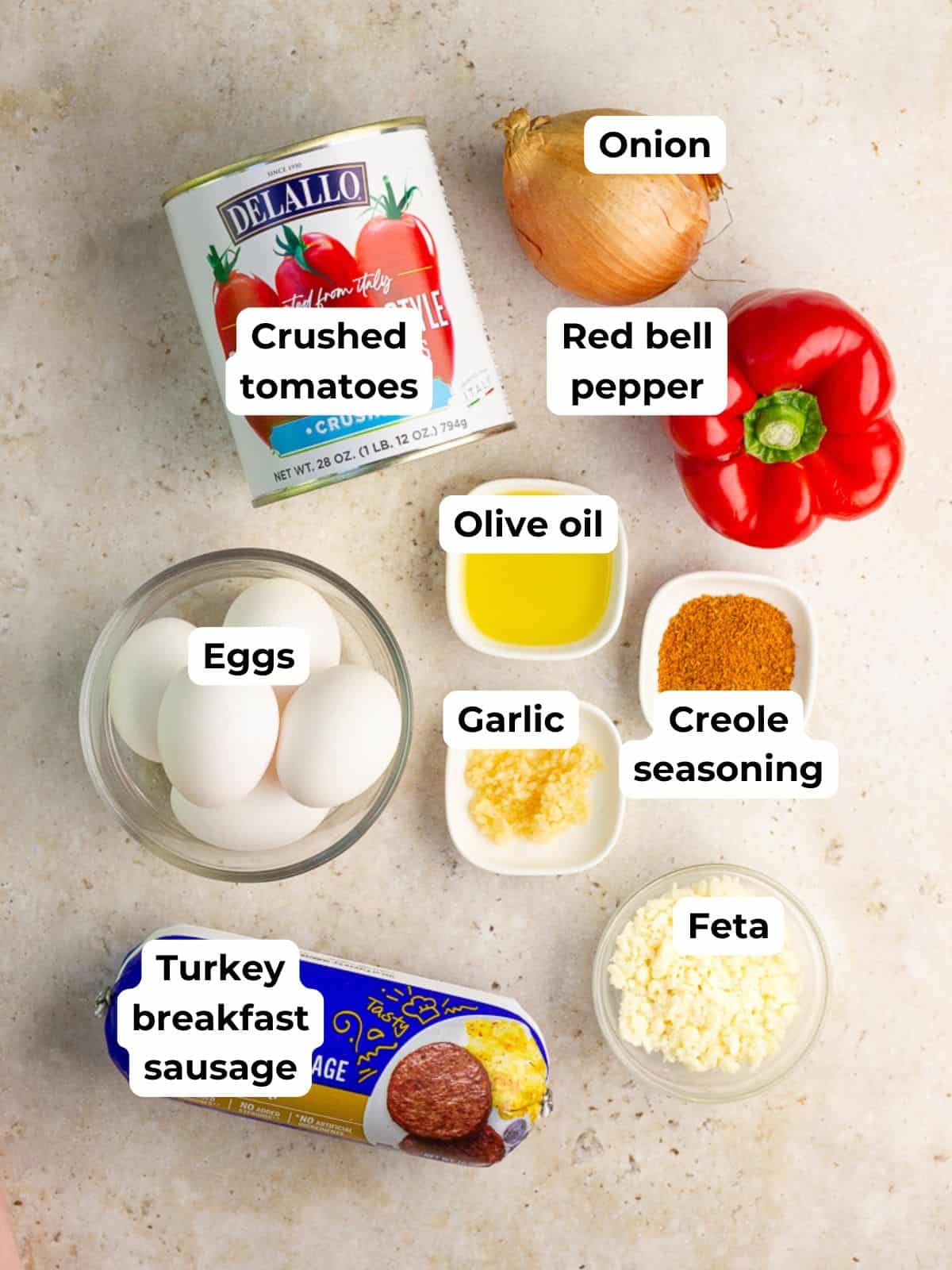 Ingredients for high protein shakshuka include crushed tomatoes, eggs, turkey sausage, red bell pepper, onion, garlic, Creole seasoning, olive oil, and feta.