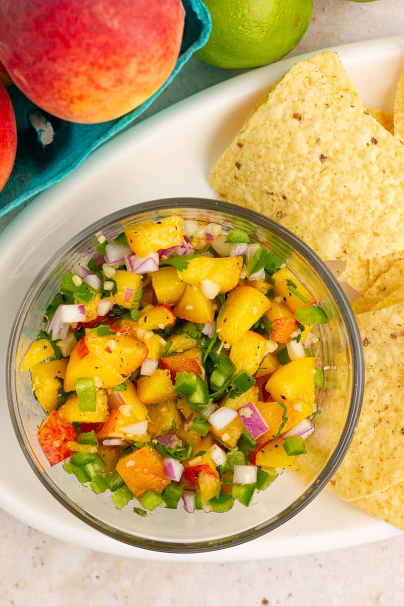 Fresh jalapeno peach salsa is served in a glass bowl with tortilla chips and summer peaches.