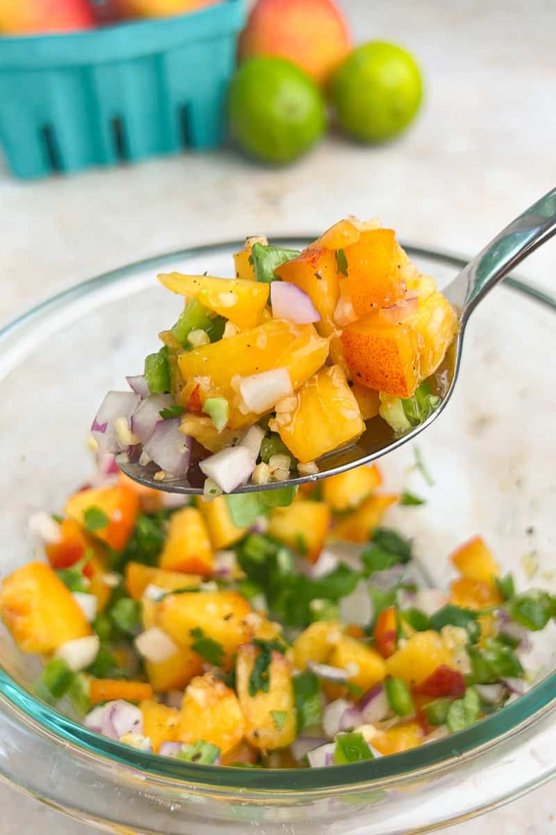 A spoonful of jalapeno peach salsa is lifted from a glass mixing bowl.