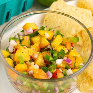 A close-up bowl of fresh jalapeno peach salsa is served with tortilla chips.