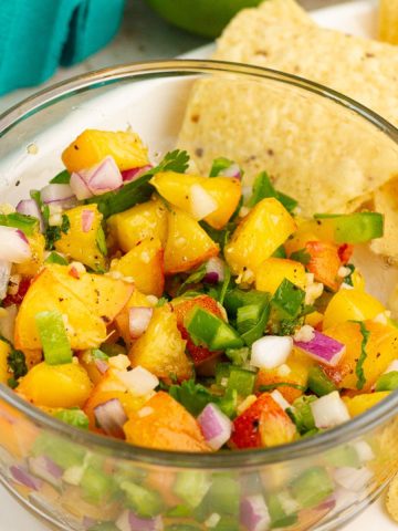 A close-up bowl of fresh jalapeno peach salsa is served with tortilla chips.