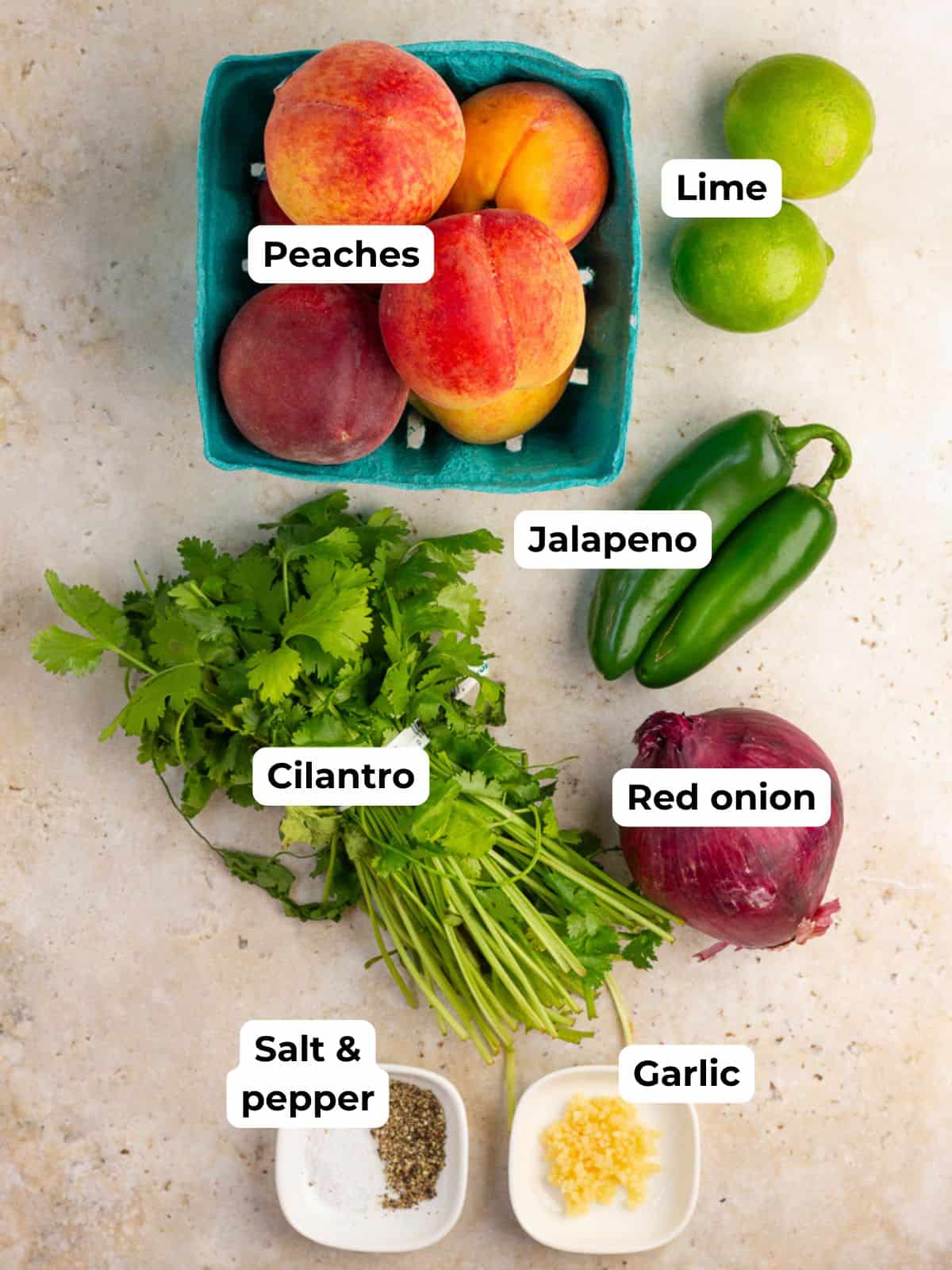 The ingredients for jalapeno peach salsa are arranged with labels on a countertop.