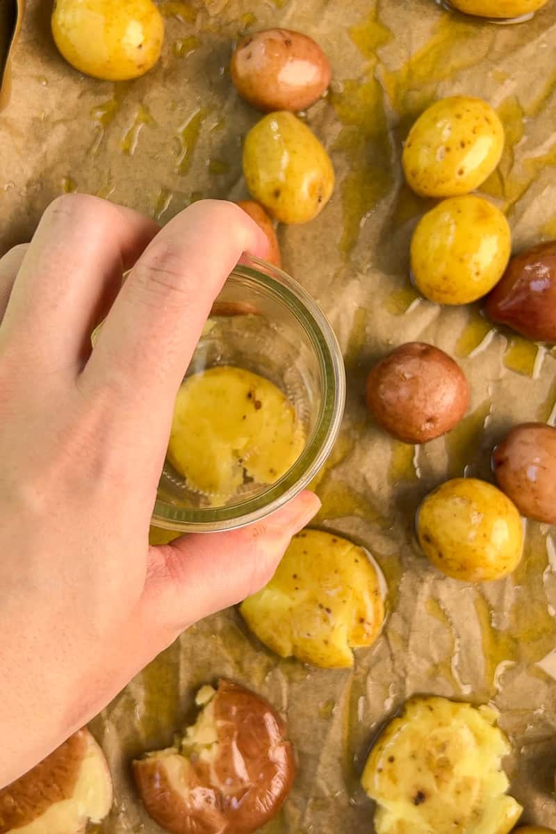 Petite potatoes are smashed with a glass on a parchment-lined baking sheet.