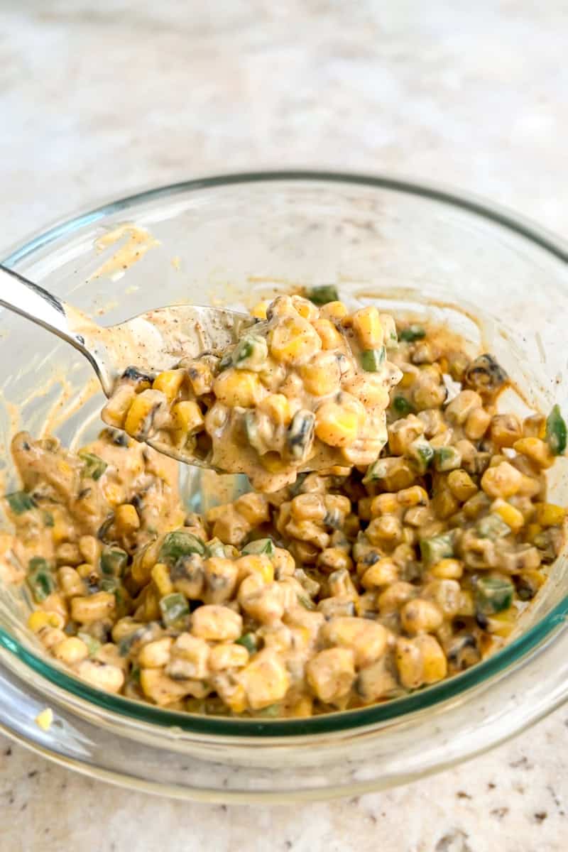 Creamy fire roasted corn topping is mixed in a glass bowl for Mexican smashed potatoes.