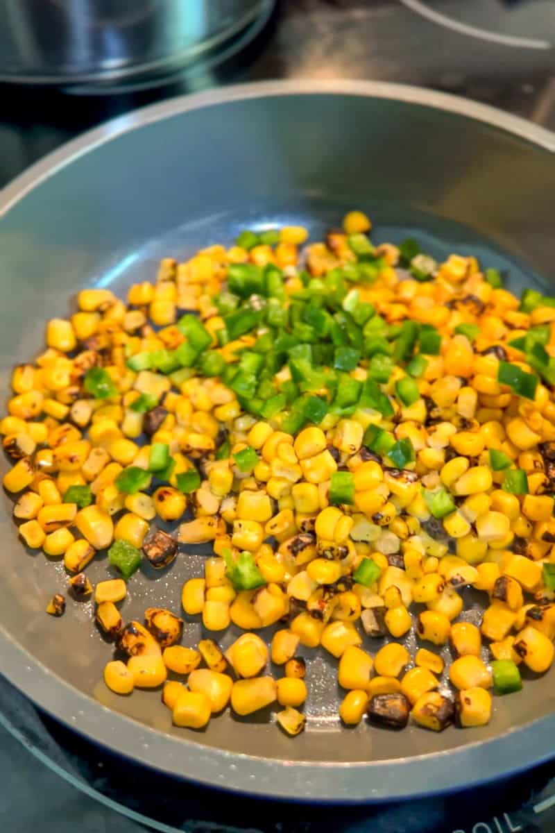 Fire roasted corn and diced jalapeño are warmed together in a skillet.
