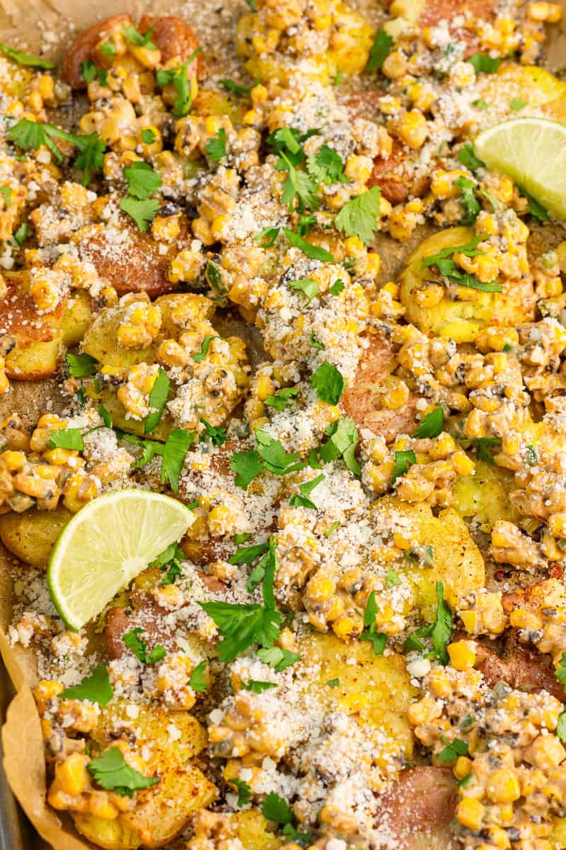 Close up of street corn smashed potatoes are topped with creamy fire roasted corn, cotija cheese, cilantro, and lime wedges.