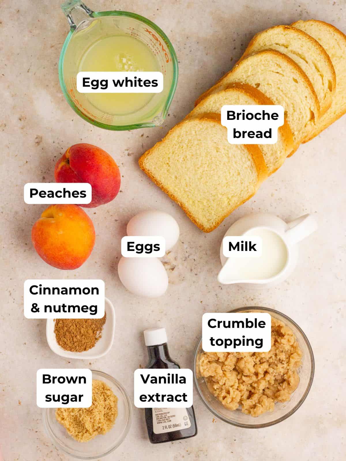 The ingredients for peach cobbler French toast casserole, including brioche, peaches, eggs, milk, cinnamon, brown sugar, vanilla, and crumb topping, are displayed on a countertop.