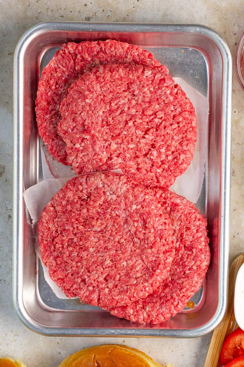 Raw burger patties sit on a tray ready to be seasoned and grilled for pimento cheese burgers.