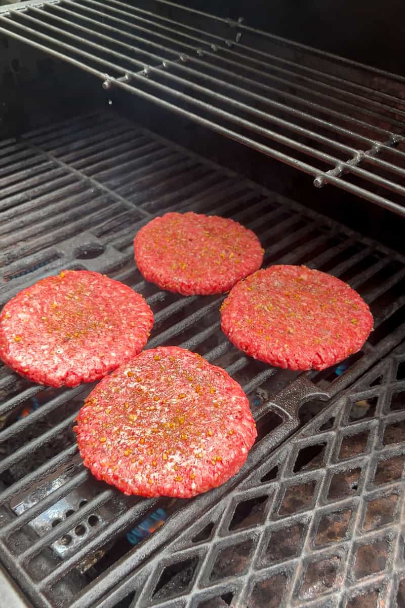 Seasoned burger patties cook on an outdoor grill before being topped with pimento cheese.