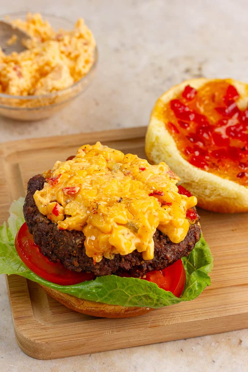 An open-faced pimento cheese burger is topped with melted pimento cheese and bacon pepper jam on a toasted bun.
