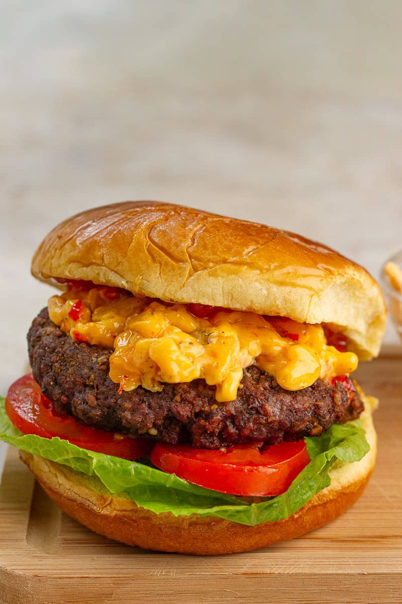 A fully assembled pimento cheese burger is stacked with lettuce, tomato, pimento cheese, and bacon pepper jam.