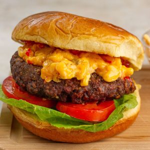A pimento cheese burger topped with bacon pepper jam sits on a toasted bun with lettuce and tomato.