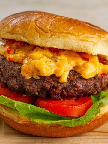 A pimento cheese burger topped with bacon pepper jam sits on a toasted bun with lettuce and tomato.