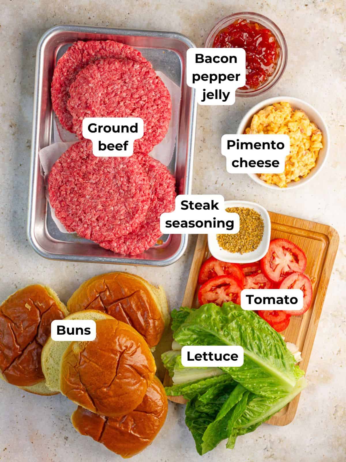 Ground beef, pimento cheese, bacon pepper jam, steak seasoning, buns, lettuce, and tomato are arranged for making pimento cheese burgers.