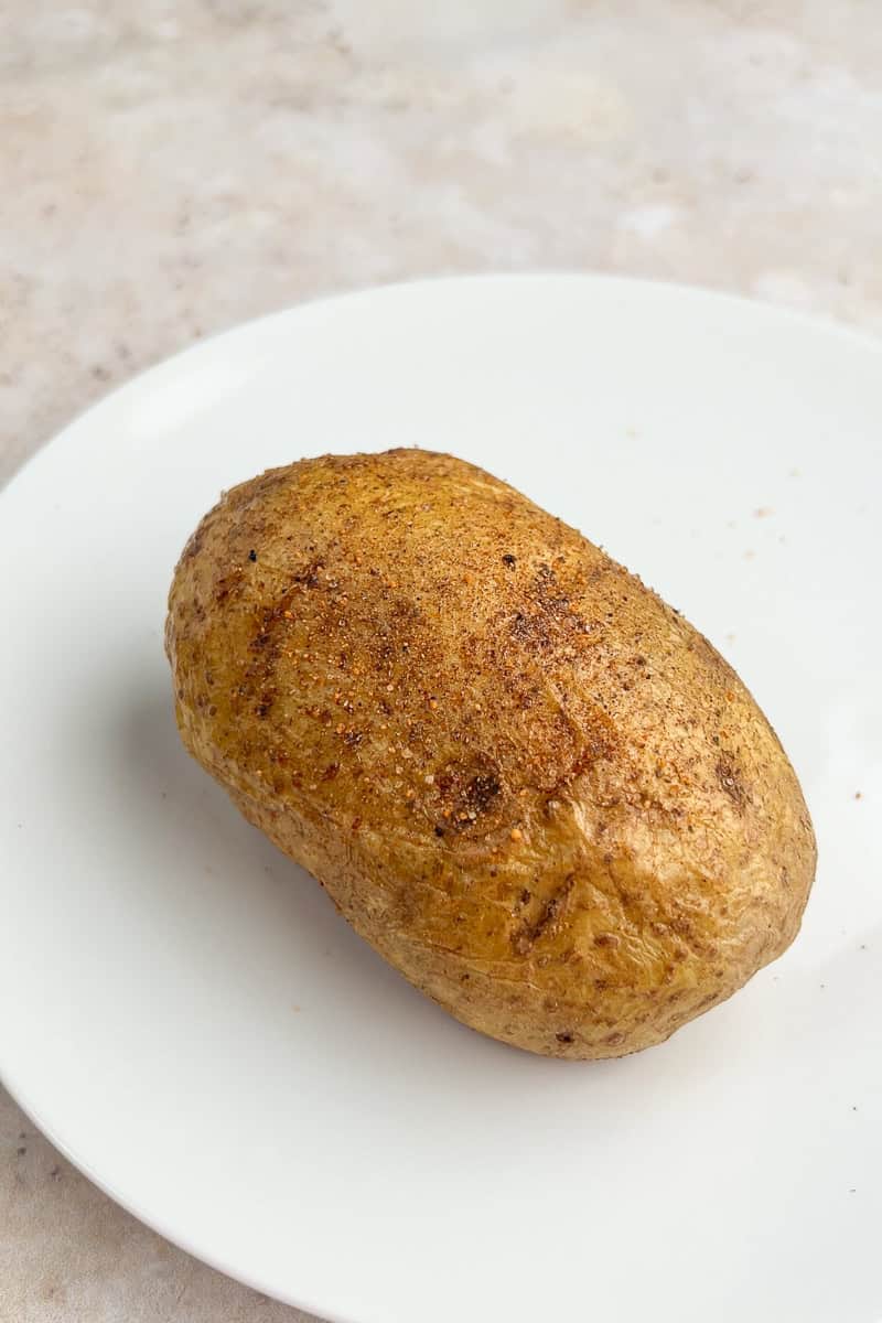 A seasoned baked potato sits on a white plate.