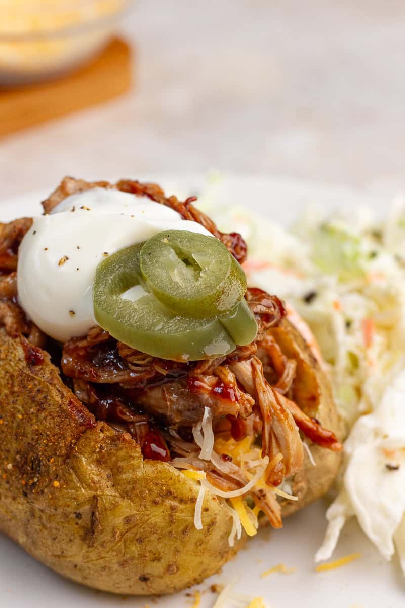 A close-up of a BBQ pulled pork baked potato with coleslaw on a white plate.