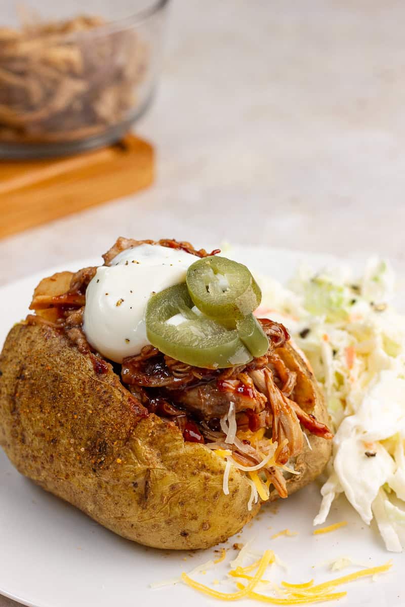 A loaded pulled pork baked potato is topped with sour cream and jalapeños.