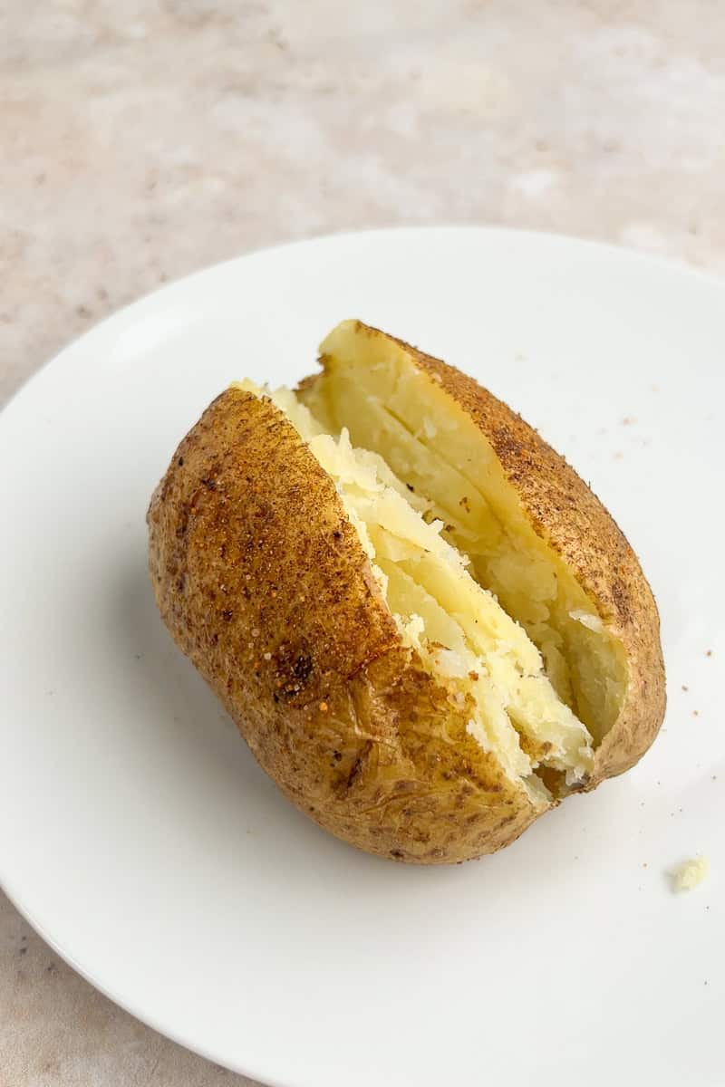 A baked potato is sliced open on a white plate.