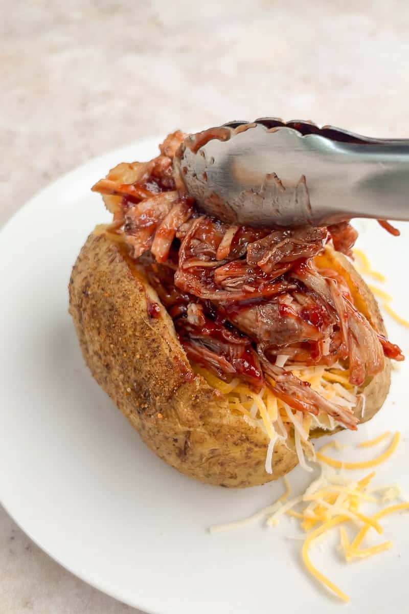 BBQ pulled pork is added to a baked potato with shredded cheese.
