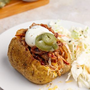 A loaded pulled pork baked potato is served with coleslaw.
