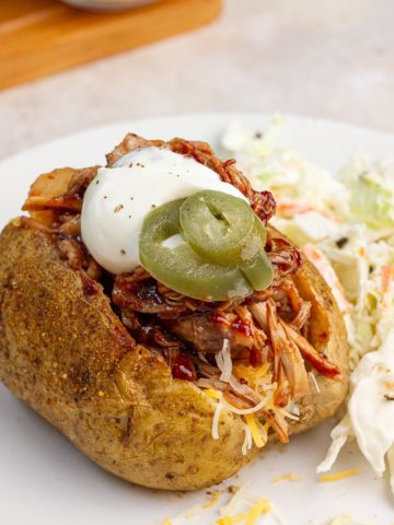 A loaded pulled pork baked potato is served with coleslaw.