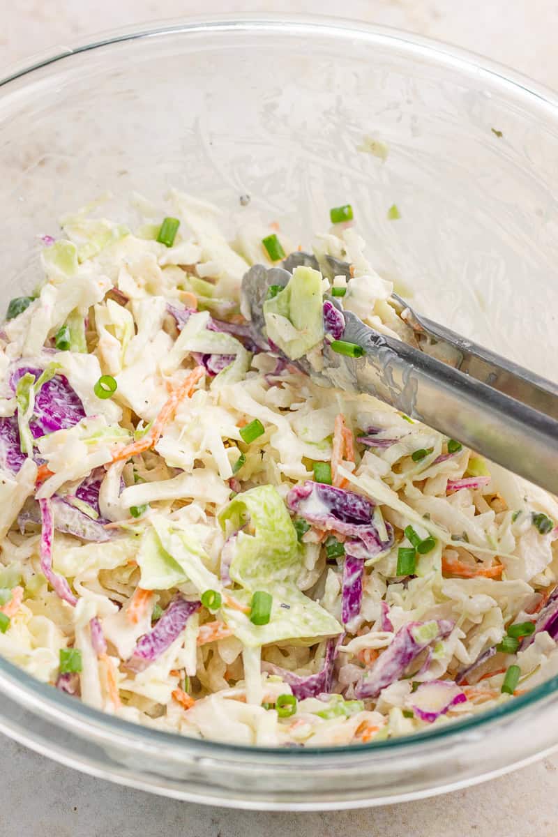 A close-up of ranch coleslaw shows colorful cabbage, carrots, and green onions.