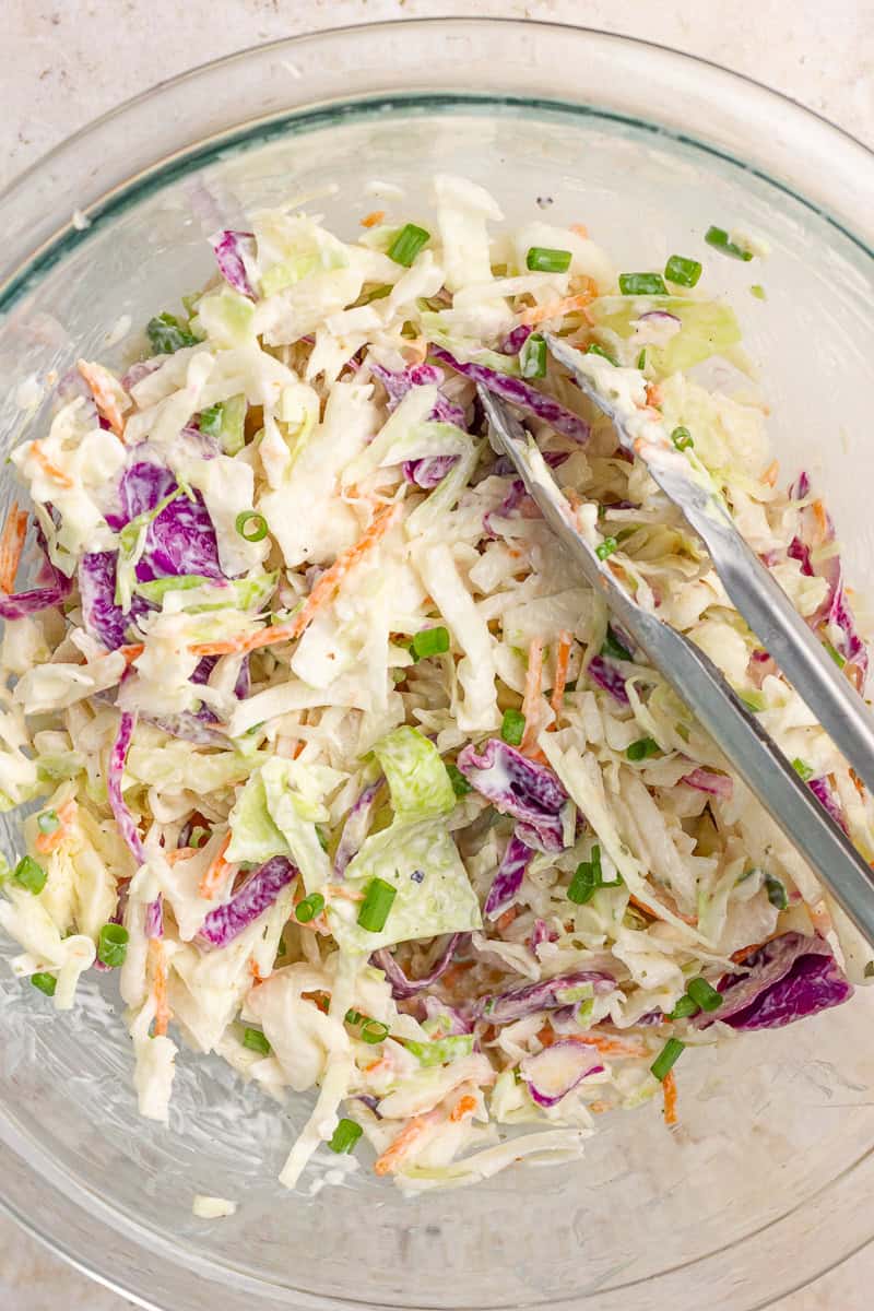 Creamy ranch coleslaw with green onions is tossed in a glass mixing bowl.